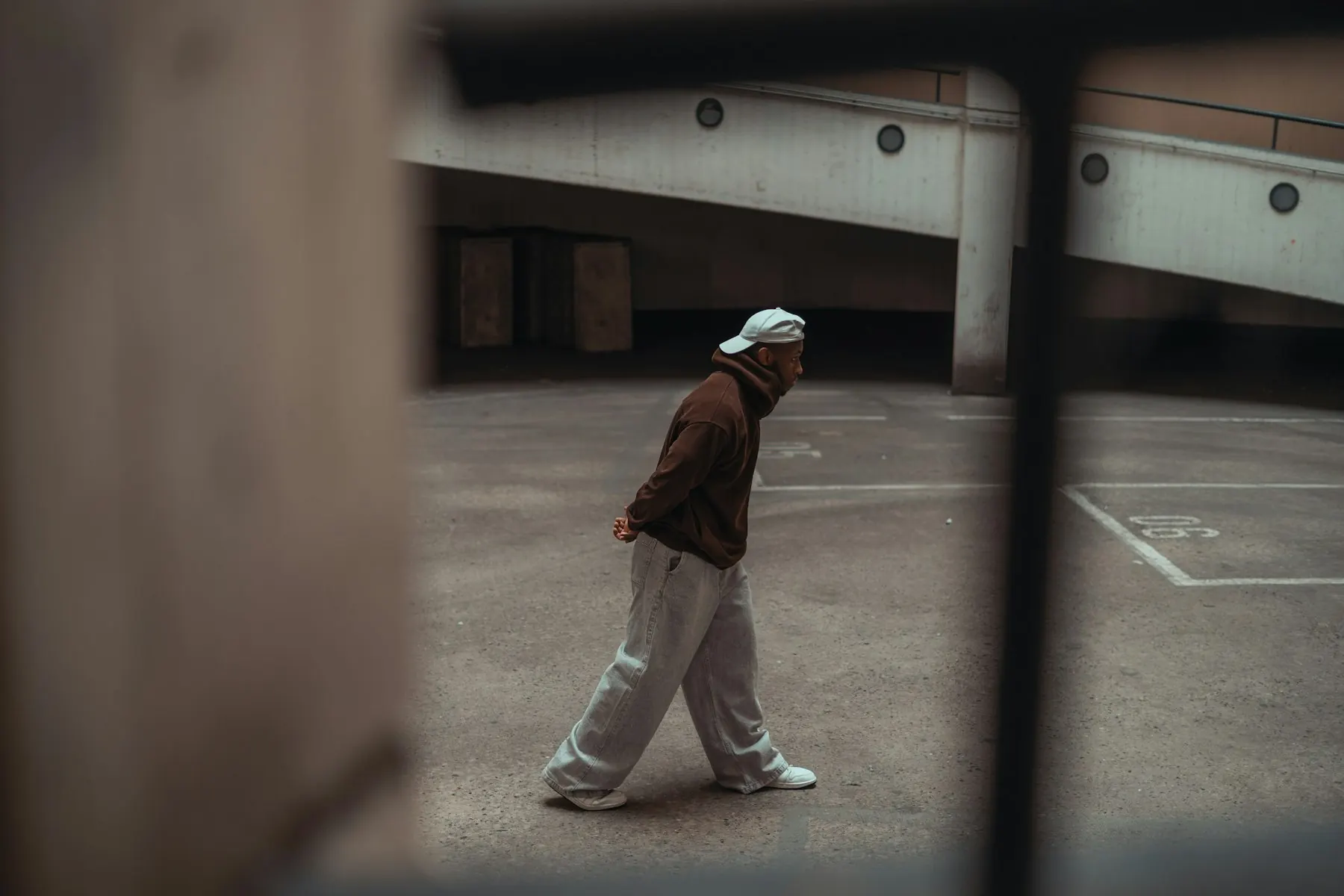 Video frame of a man walking in a cap, hoodie, wide jeans and sneakers